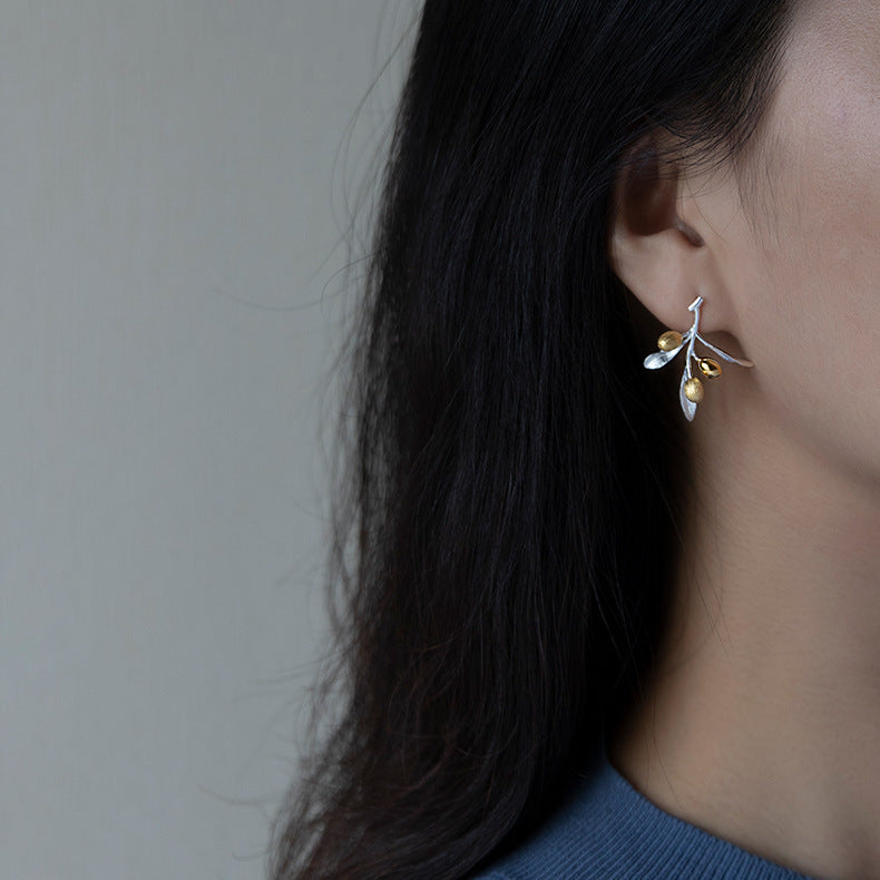 Close-up of a person wearing a delicate silver and gold earring against a neutral background