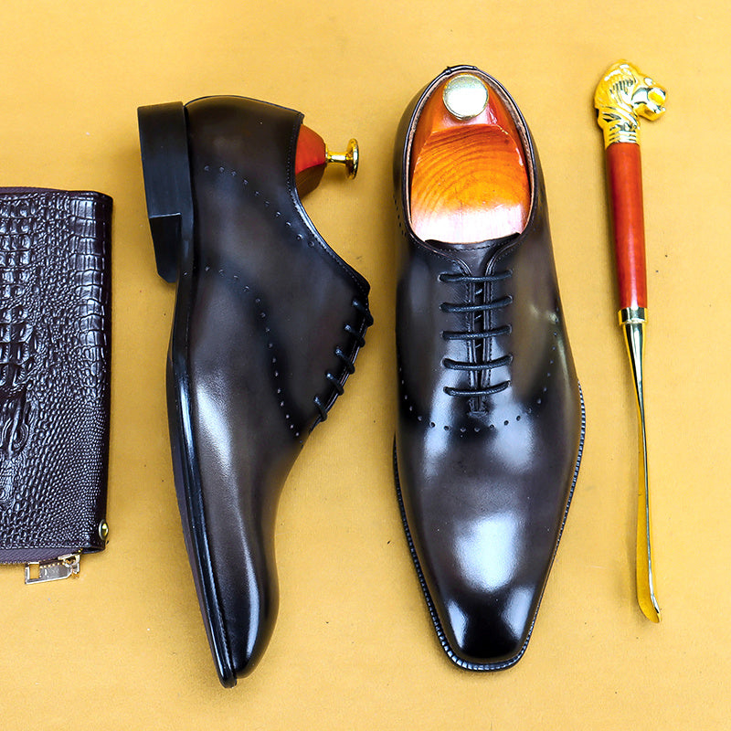 Pair of black dress shoes with a shoe horn and wallet on a yellow background