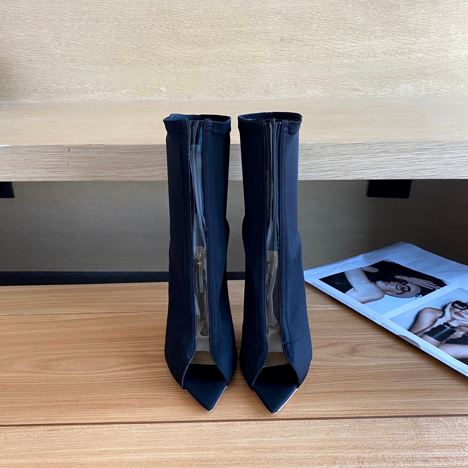 Pair of navy blue high-heeled shoes on a wooden surface with a magazine in the background.