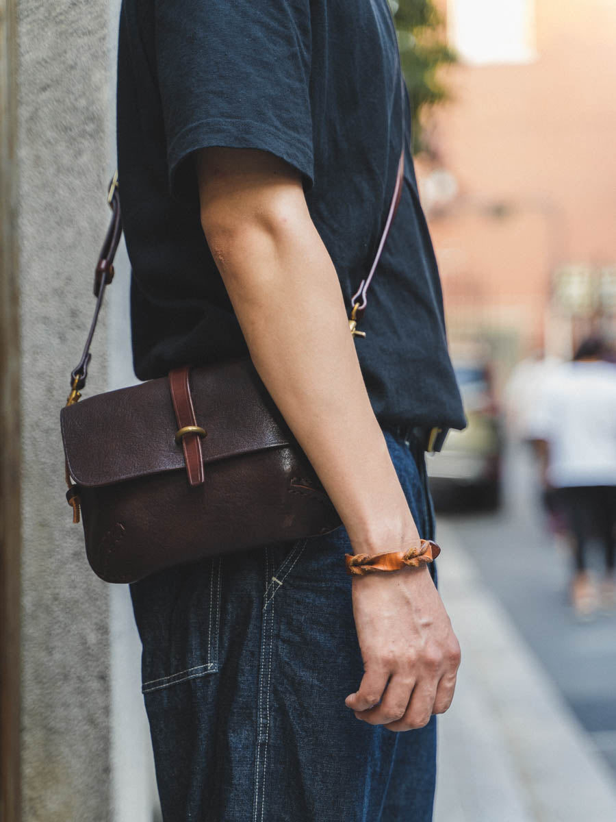 Person holding a brown leather bag with a blurred street background