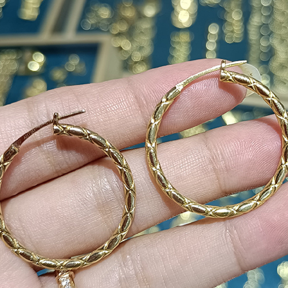 Gold hoop earrings held between fingers with a blurred decorative background