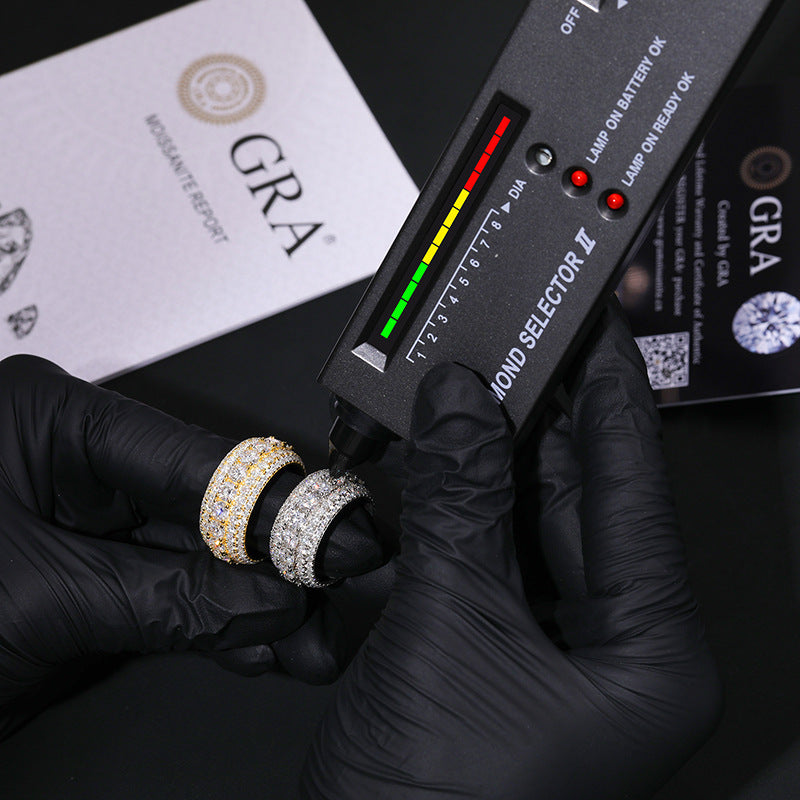 Diamond selector tool with two diamond rings held by gloved hands, with GRA branding in the background.