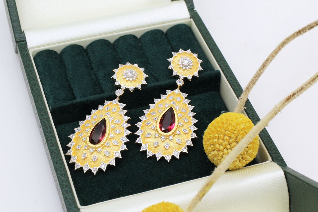 Gold earrings with red gemstones in a green jewelry box on a white background