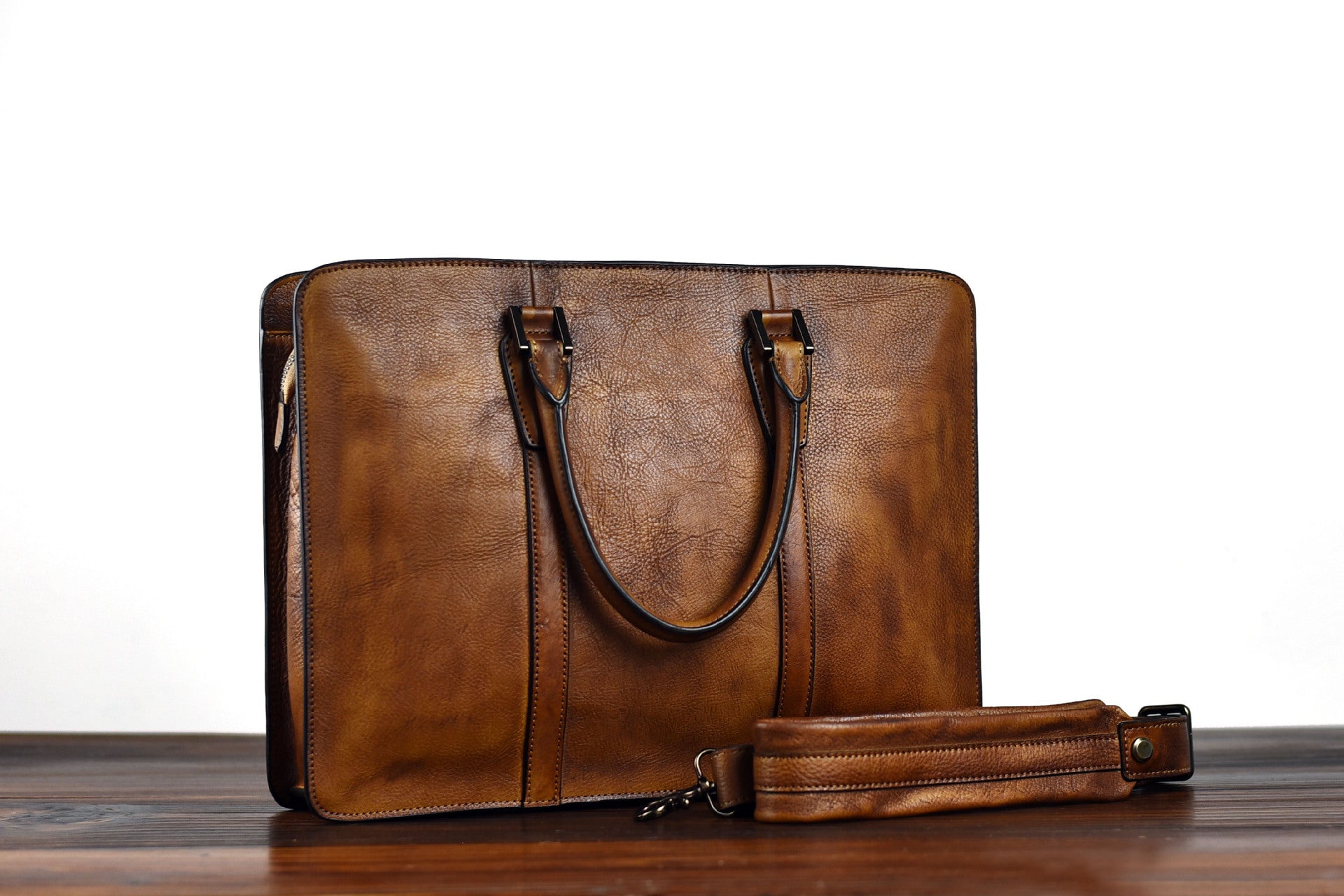 Brown leather briefcase with a strap on a wooden surface