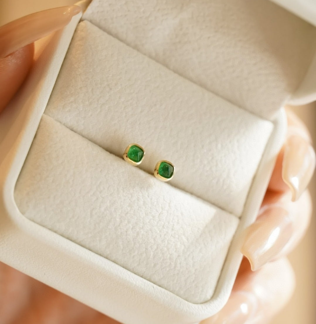 Green gemstone earrings in a jewelry box held by a hand