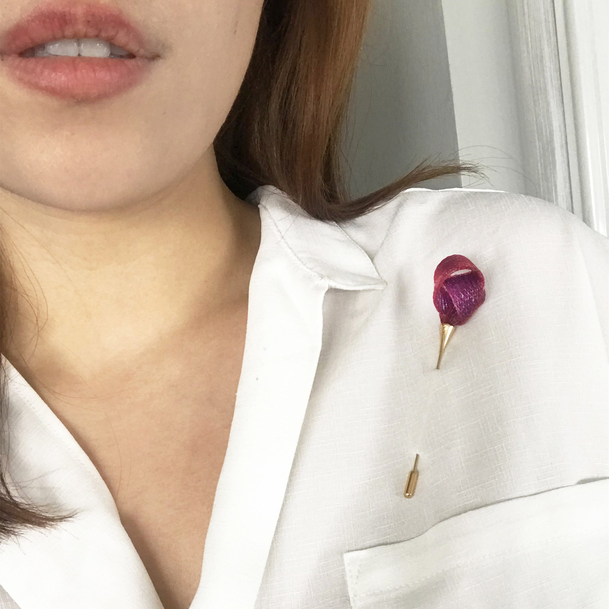 Close-up of a person wearing a white shirt with a pink brooch.