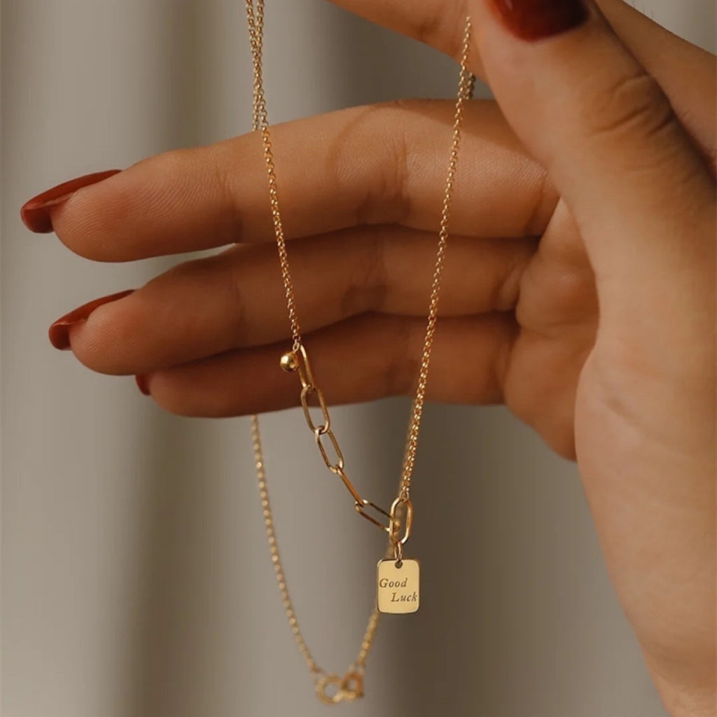 Hand holding a gold necklace with a tag against a neutral background