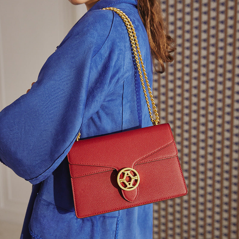 Person wearing a blue coat with a red handbag featuring a gold chain strap and clasp.