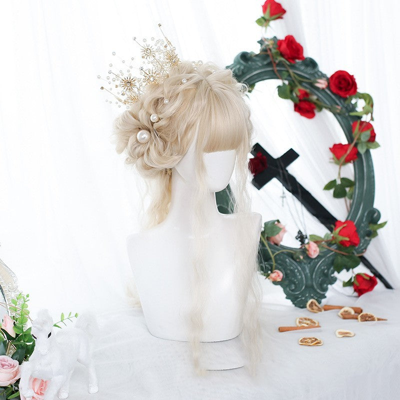 Blonde wig with decorative hairpiece on a mannequin head, with decorative wreath and flowers in the background.