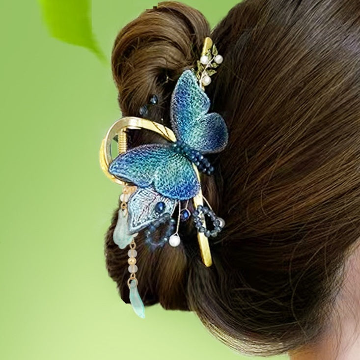 Decorative hair clip with butterfly design in a person's hair against a green background