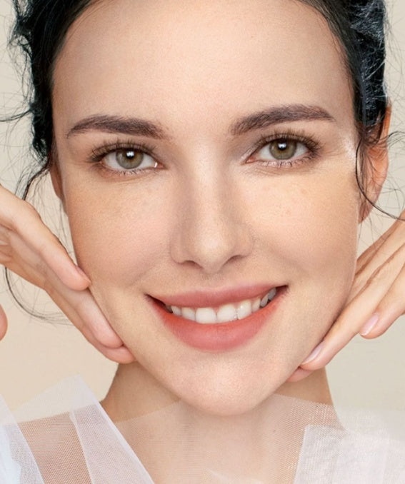 Woman with a soft smile and gentle touch on her face against a neutral background