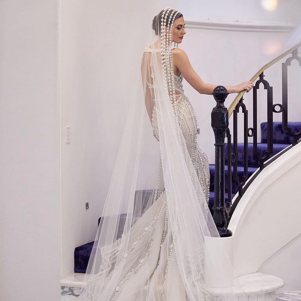 Woman in a white beaded gown with a long train standing on a staircase.