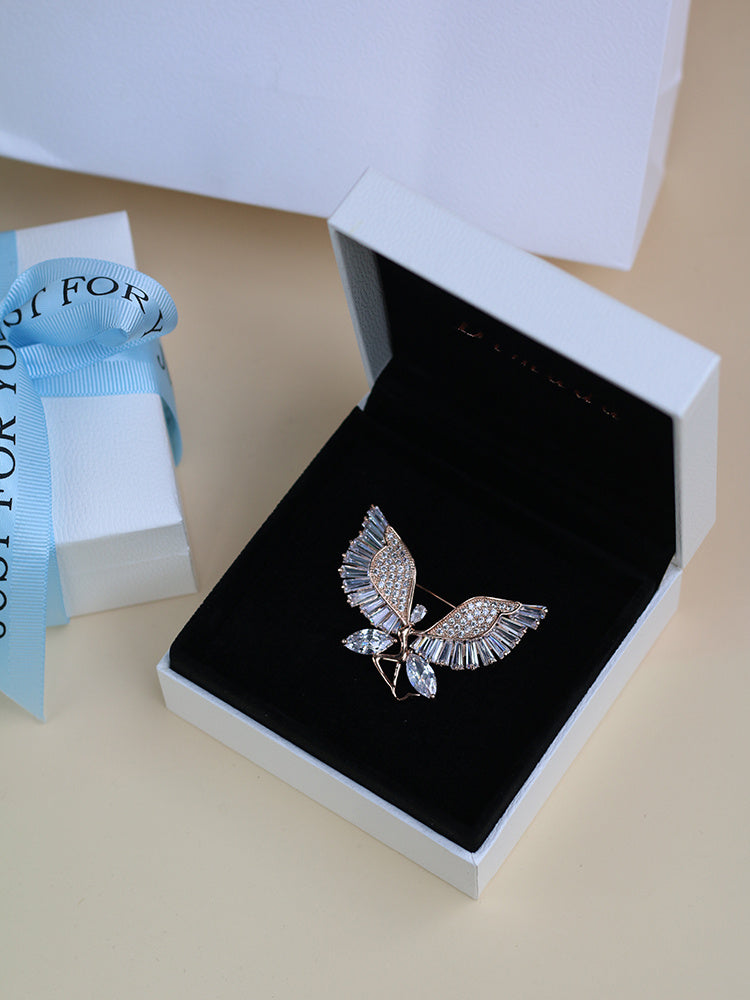 Silver butterfly brooch in an open jewelry box with a blue ribbon in the background.