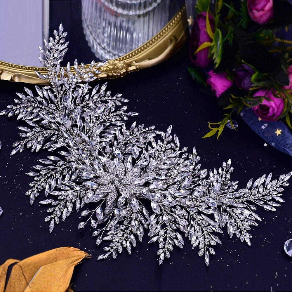 Decorative silver leaf-like piece with crystals on a dark surface with a mirror and flowers in the background.