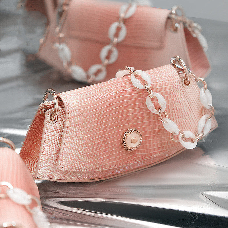 Pink handbag with a chain detail on a reflective surface