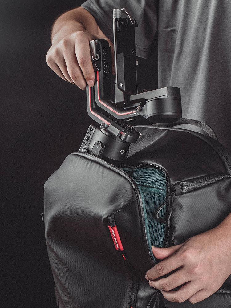 Person holding a backpack with a camera stabilizer attached on a dark background