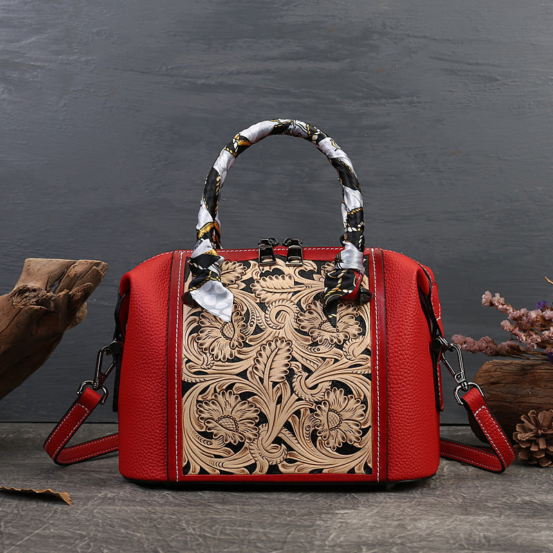Red handbag with intricate floral tooled leather design on a dark background