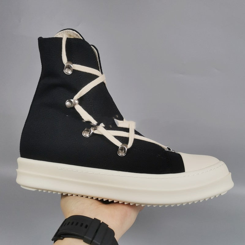 Black high-top sneaker with white laces and sole held by a hand against a gray background