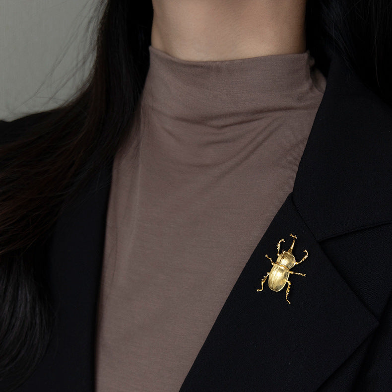 Gold beetle brooch on a black blazer with a brown shirt underneath.