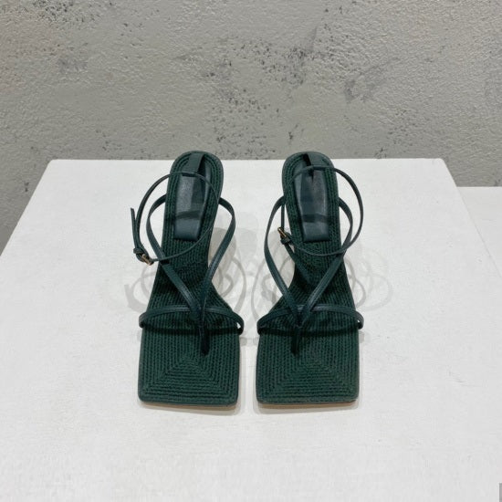 Pair of green high-heeled sandals on a white surface with a gray background