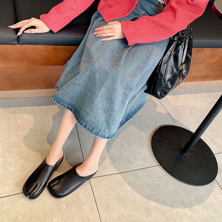 Person wearing a red sweater, blue denim skirt, and black shoes sitting on a bench.
