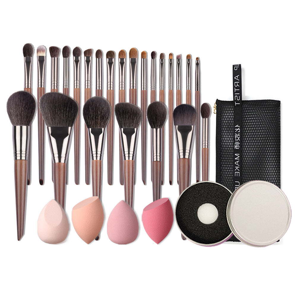 Makeup brush set with pink and beige sponges, a black and silver compact mirror, and a black makeup bag on a white background.