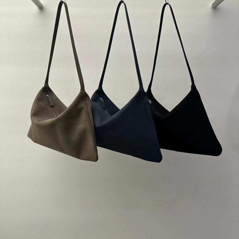 Three handbags in brown, blue, and black hanging against a white wall.