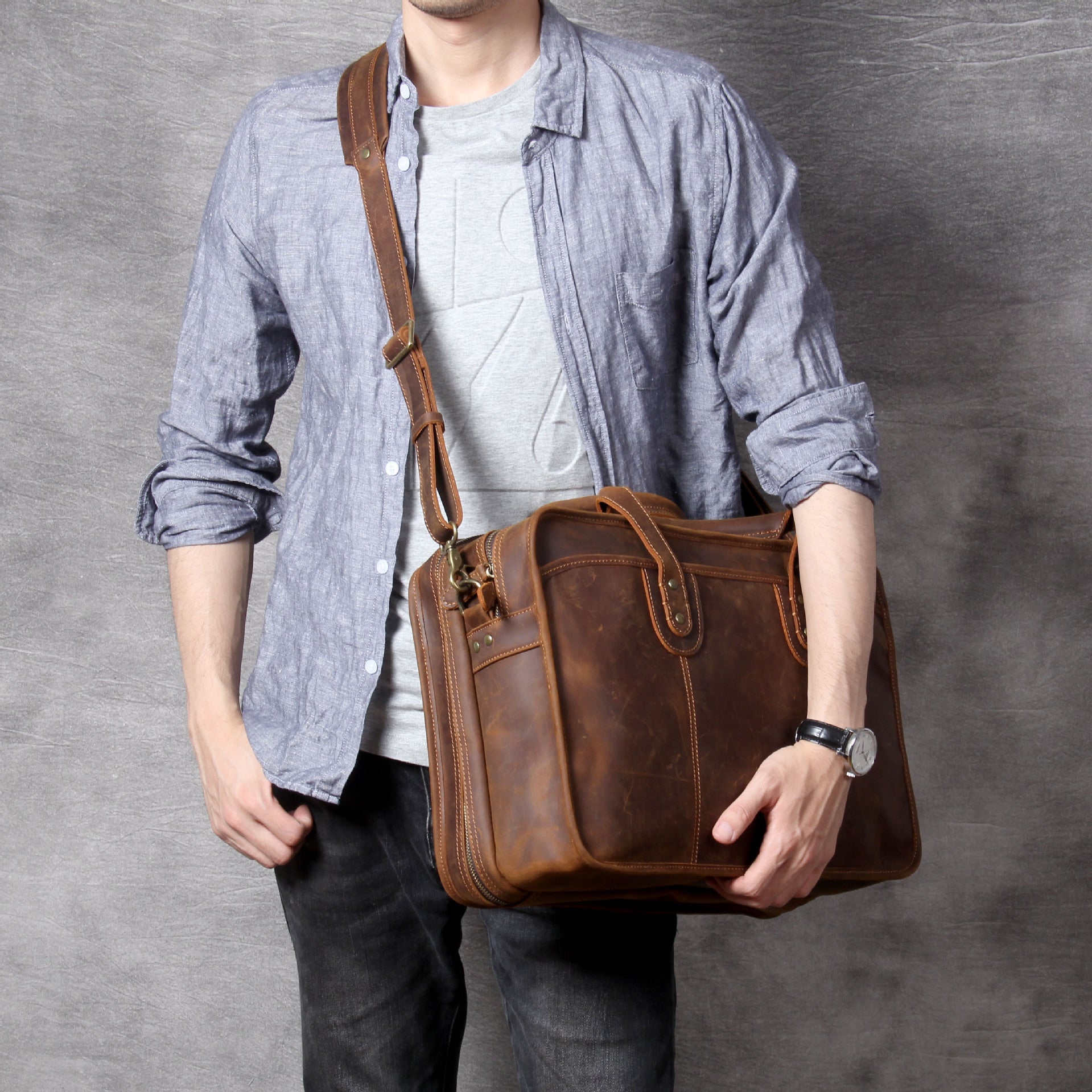 Person holding a brown leather bag against a gray background