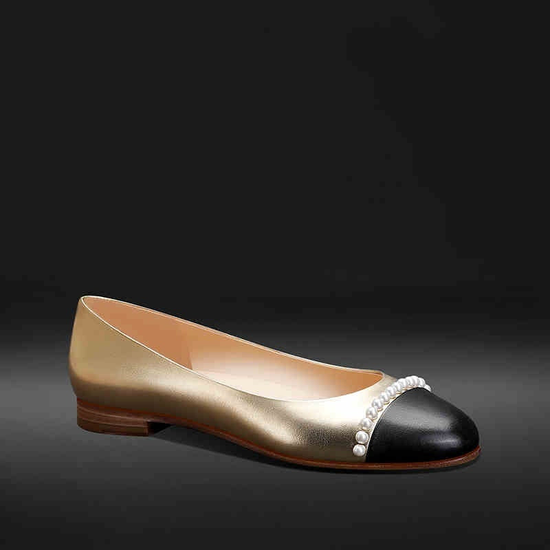 Gold and black flat shoe with pearl embellishments on a dark background