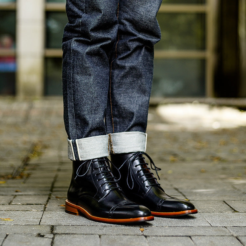 Person wearing black leather boots and rolled-up jeans on a paved surface.