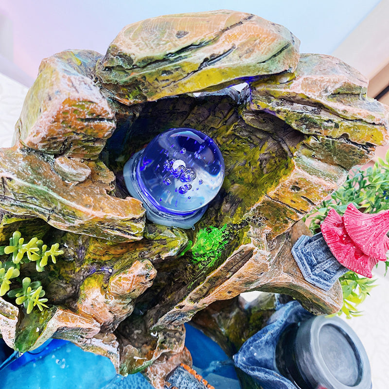 Decorative rock with a blue light inside, surrounded by artificial plants.