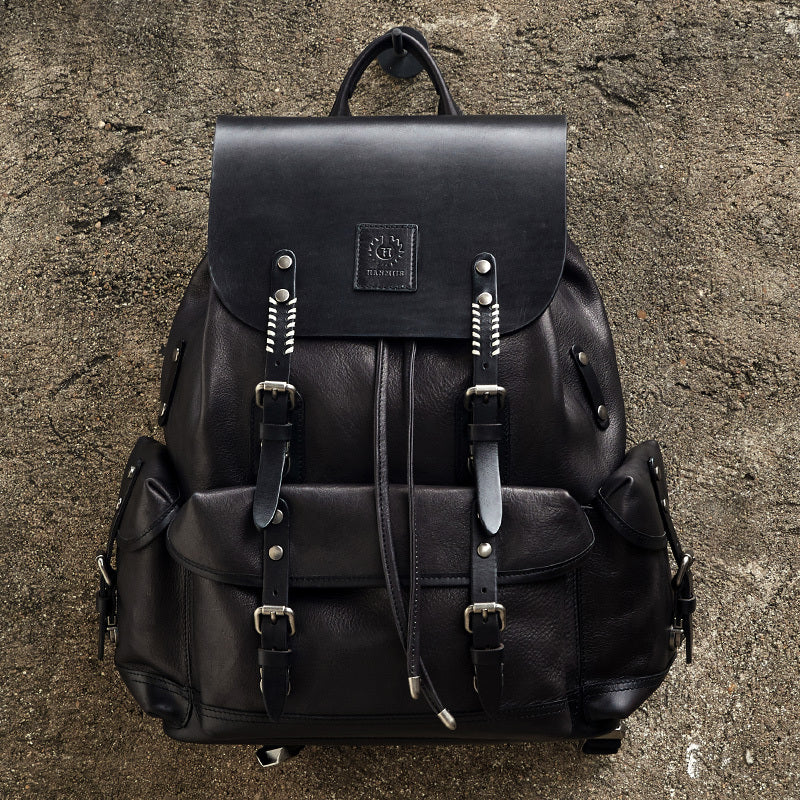 Black leather backpack with metal buckles on a textured surface