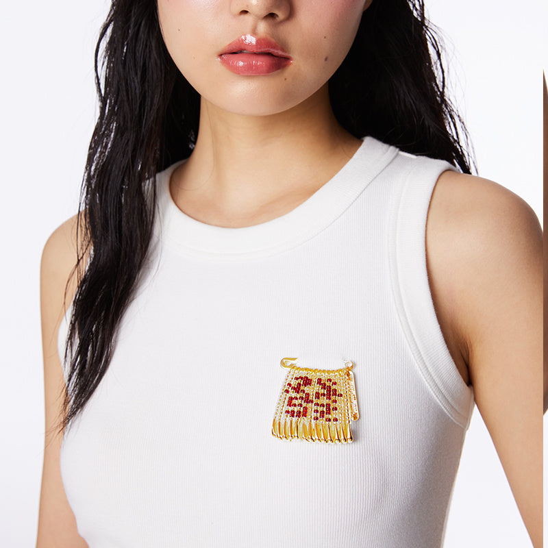 Woman wearing a white sleeveless top with a decorative brooch on a plain background