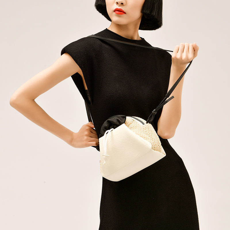 Woman holding a cream-colored bag with a black strap against a plain background