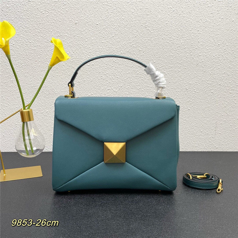 Teal handbag with gold accents on a gray surface with yellow flowers in the background