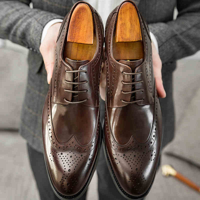 Brown leather dress shoes with wooden soles held by a person wearing gray pants.
