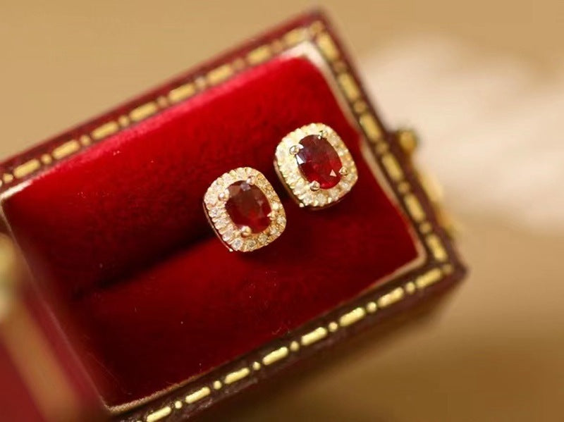 Pair of red gemstone earrings in a gold box on a beige background