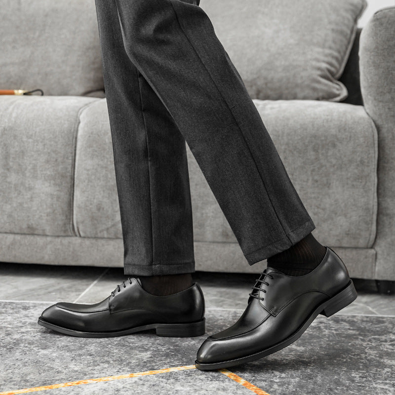 Person wearing black dress shoes and gray pants sitting on a gray couch.