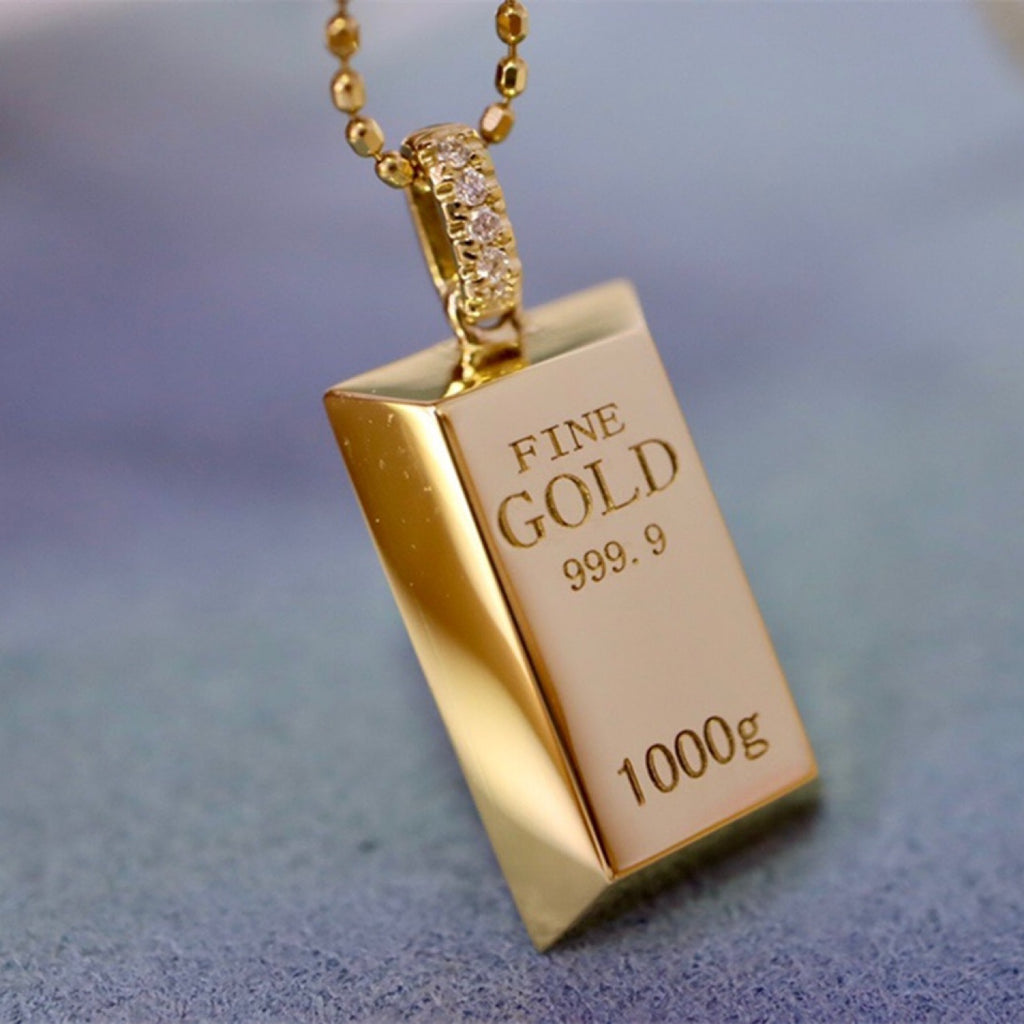 Gold pendant shaped like a gold bar with 'FINE GOLD 999.9' engraving on a blurred background