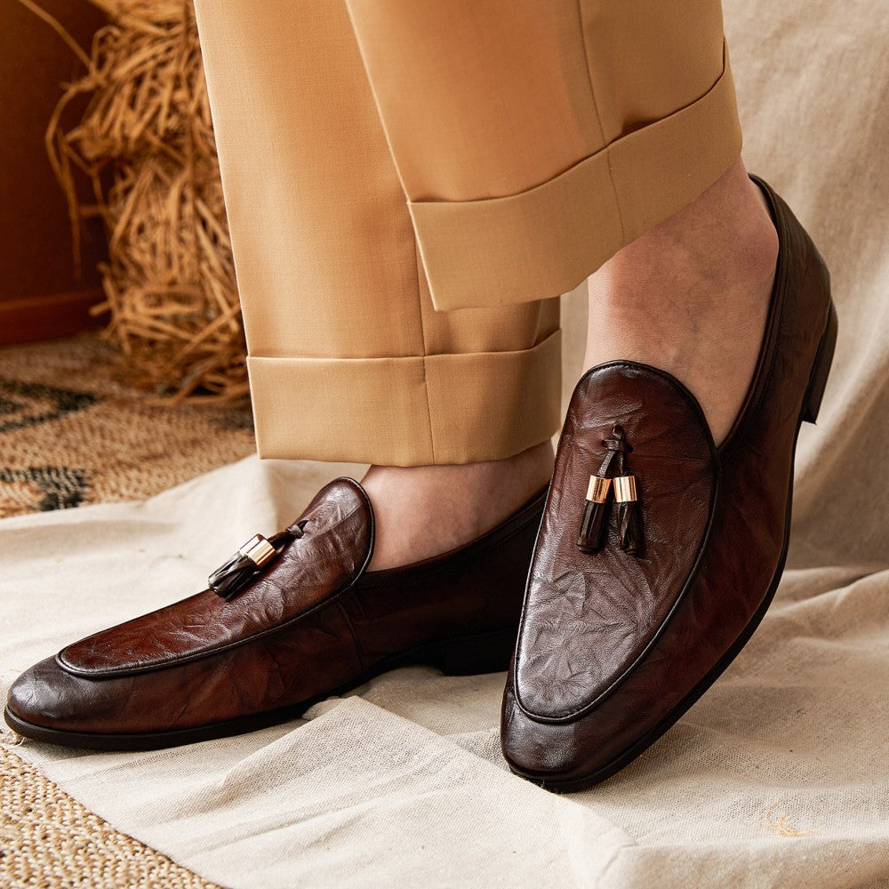Brown loafers with tassels worn with beige pants on a neutral background