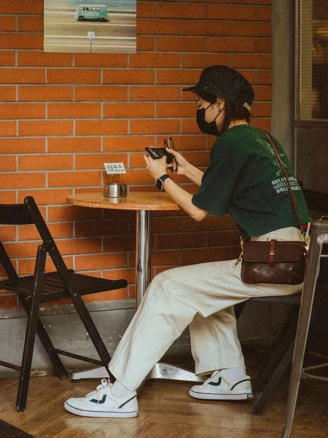 Person sitting at a table in a cafe, using a phone with a brick wall background