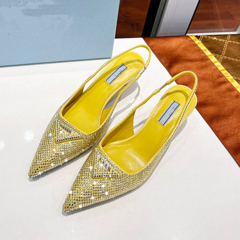 Pair of yellow pointed-toe shoes with rhinestone details on a white surface.