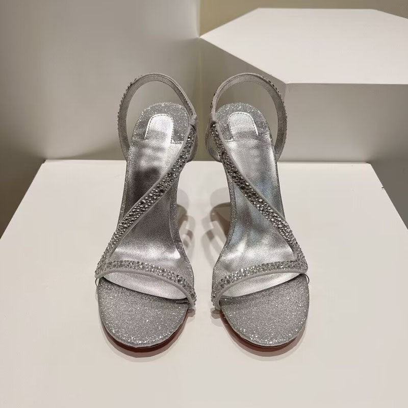 Pair of silver glitter high-heeled sandals on a white surface.