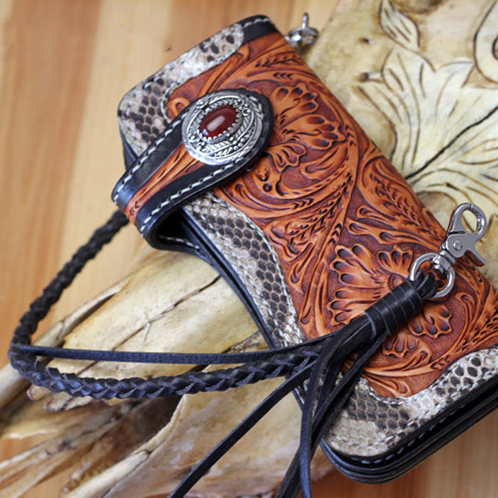 Handcrafted leather phone case with intricate designs and braided black cord on a wooden surface.