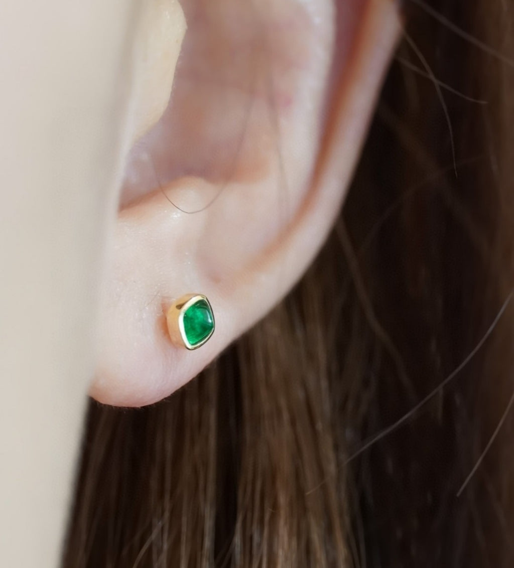 Close-up of an ear wearing a gold earring with a green gemstone.