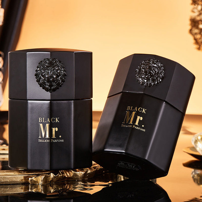Two black perfume bottles with gold text on a reflective surface.