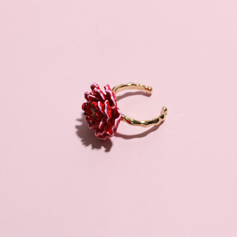Gold ring with a red flower design on a pink background