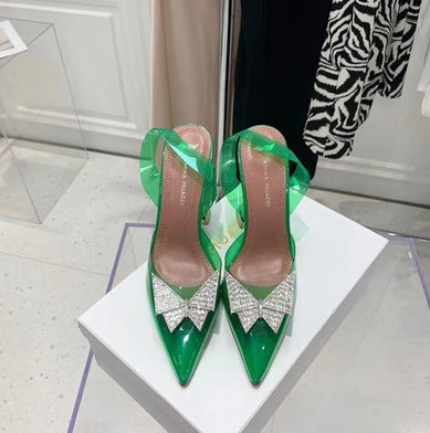 Green high-heeled shoes with crystal bows on a white platform.