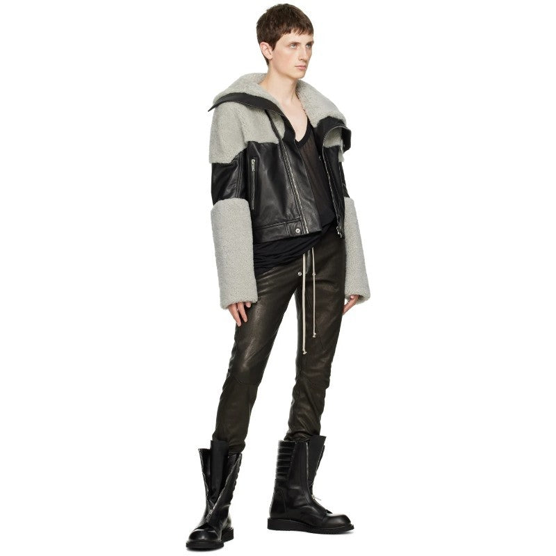 Person wearing a two-tone jacket with black and gray sections, black pants, and black boots on a white background.