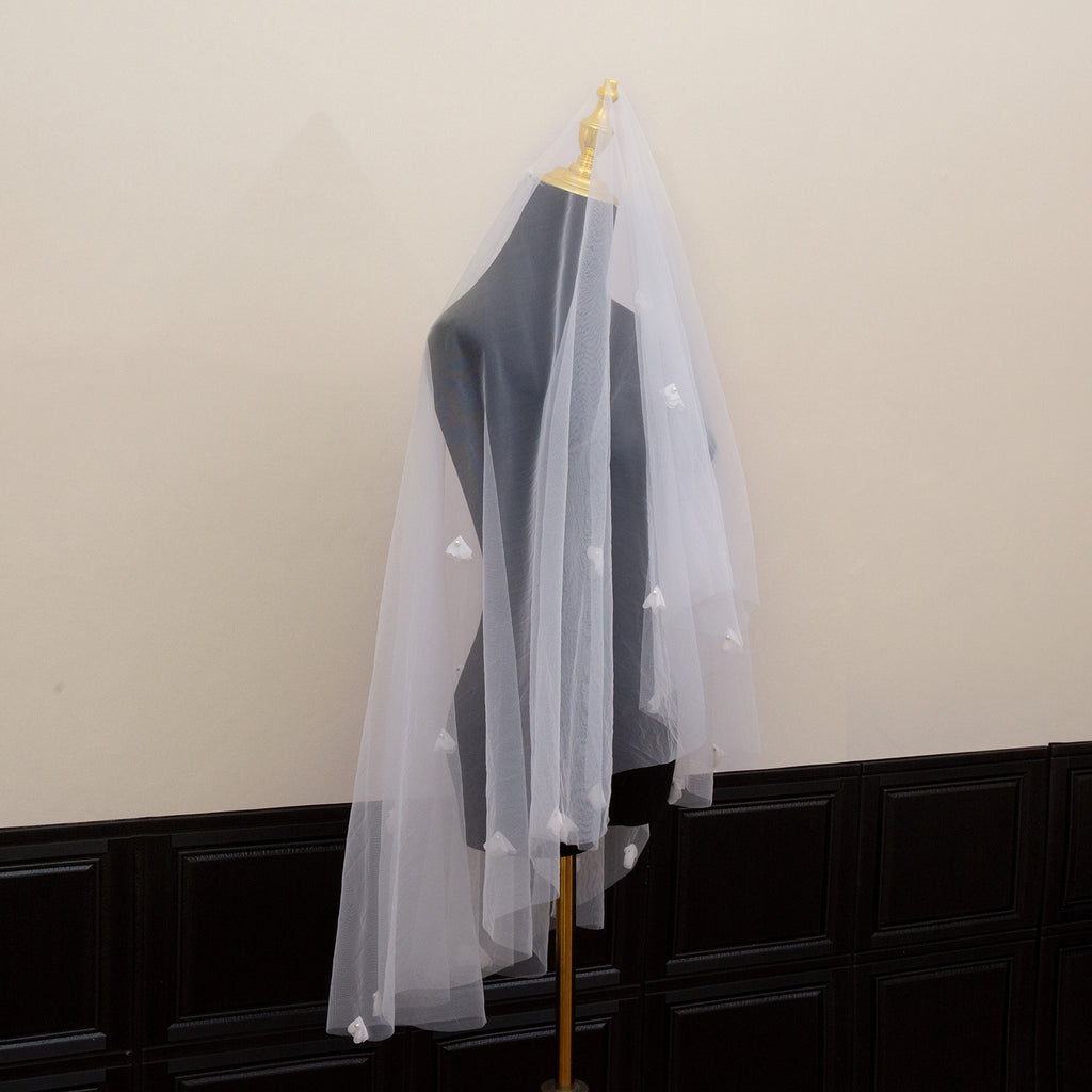 White veil with star patterns on a mannequin against a neutral wall.